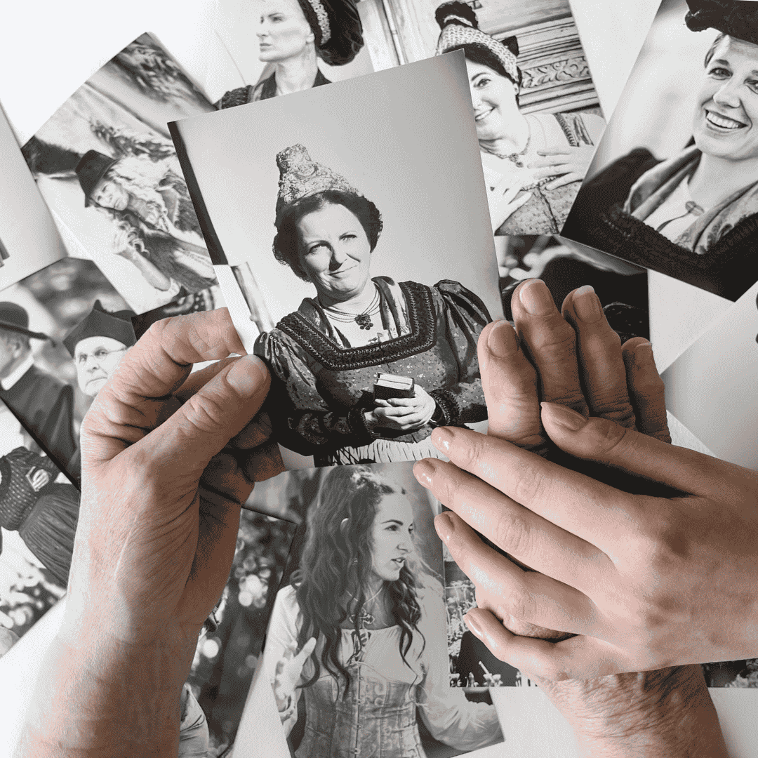 Zwei Frauenhände halten ein Bild von früher in der Hand. Auf dem Tisch verteilt, sind ganz viele weitere Fotos.